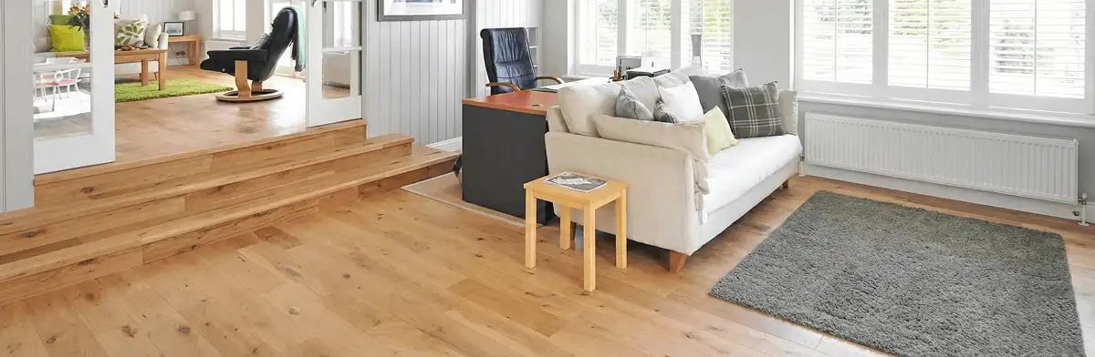A modern living room with professionally installed laminate flooring, a beige sofa, a small side table, a gray rug, and large windows with white shutters in Ann Arbor, MI